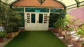 A conservatory with a green artificial turf path leading to a white door, surrounded by potted plants. - Royal Motel Executive (Islamabad)
