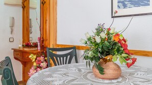 Et spisebord med hvide blonde, en kobbervase med blomster, et træskab og et billede i ramme på væggen.