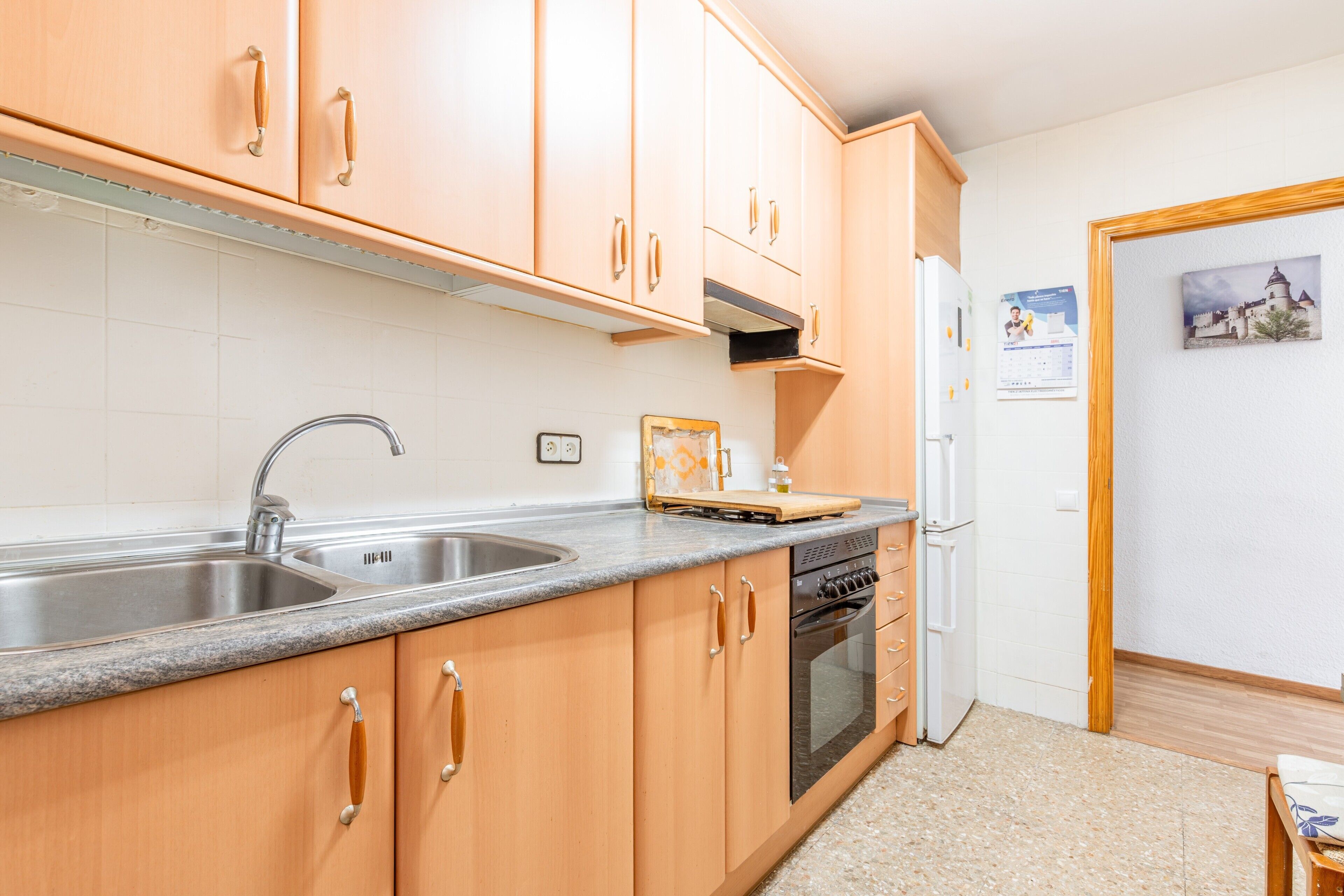 A kitchen with wooden cabinets, a stainless steel sink, a built-in oven, and a refrigerator.