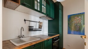 Eine Küche mit grünen Schränken, einer Holzarbeitsplatte, einem Spülbecken, einem Backofen und einem Bild an der Wand.