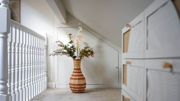A hallway with a white railing, a woven vase with flowers, and a white door with a handle. - Period Character Cottage Haworth (Haworth)