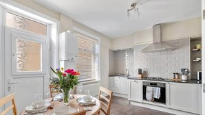 A modern kitchen with white cabinets, a stove, and a dining area with a table set for two. - Period Character Cottage Haworth (Haworth)