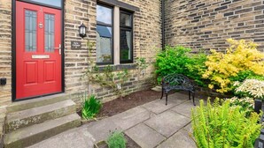 A brick building with a red door, a bench, and various plants. - Period Character Cottage Haworth (Haworth)