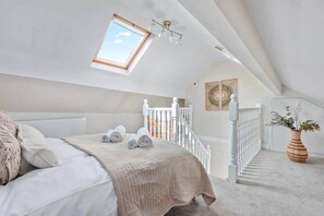 Ein Schlafzimmer mit Dachfenster, einem Bett mit zusammengerollten Handtüchern, einer Treppe und einer Pflanzvase.