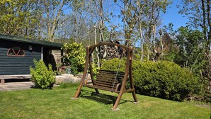 Un columpio de madera en un patio cubierto de césped, con una casa al fondo.