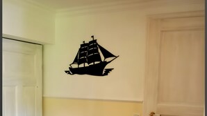 Una habitación de esquina con un banco blanco, un adhesivo en la pared con un barco y una puerta cerrada.
