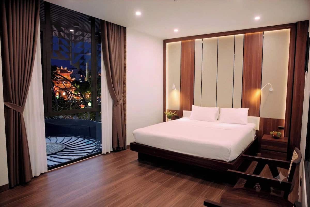A hotel room with a large bed, wooden headboard, two bedside lamps, a nightstand, and a view of a traditional building outside.