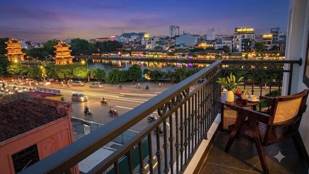 A balcony with a view of a cityscape, including a river, traditional pagoda, and modern buildings. - Kevin Hung Hotel (Hoa Lu)