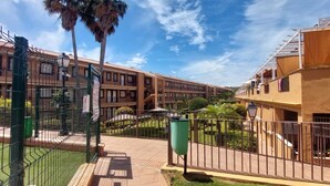 A courtyard with a fenced area, palm trees, and a building with a tiled roof. - Suite Marina Sol (Casares Costa)