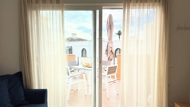 A room with a sofa, a sliding glass door to an outdoor patio, and a wooden cabinet. - Suite Marina Sol (Casares Costa)
