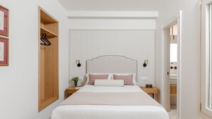 A bedroom with a bed, bedside tables, a nightstand, a wall-mounted shelf, and a door leading to another room. - Cozy lodging in Málaga (Málaga)
