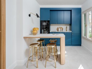 A kitchen with blue cabinets, a white countertop, and three gold stools. - Cozy lodging in Málaga (Málaga)
