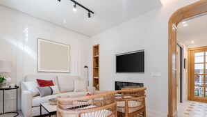 A modern living room with a white sofa, two wicker chairs, a flat-screen TV, and a bookshelf. - Cozy lodging in Málaga (Málaga)