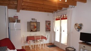 Una sala de estar con un sofá, una mesa de comedor con sillas, un televisor sobre un mueble bajo y una ventana con cortinas.