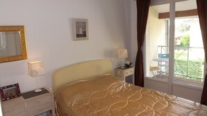 Un dormitorio con cama, mesita de noche, lámpara, espejo y ventana con cortinas.