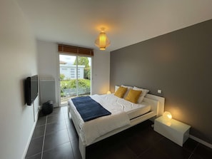 A bedroom with a bed, bedside lamps, a television, and a sliding glass door to the outside. - Modern house, private pool - 6 guests (Léon)