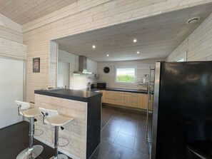A modern kitchen with a central island, bar stools, a refrigerator, and a window providing natural light. - Modern house, private pool - 6 guests (Léon)
