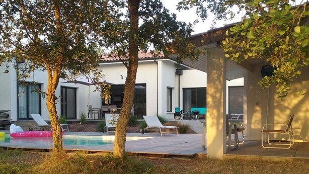 Ett modernt utomhusområde med pool, solstolar, en grill och en överbyggd sittplats.