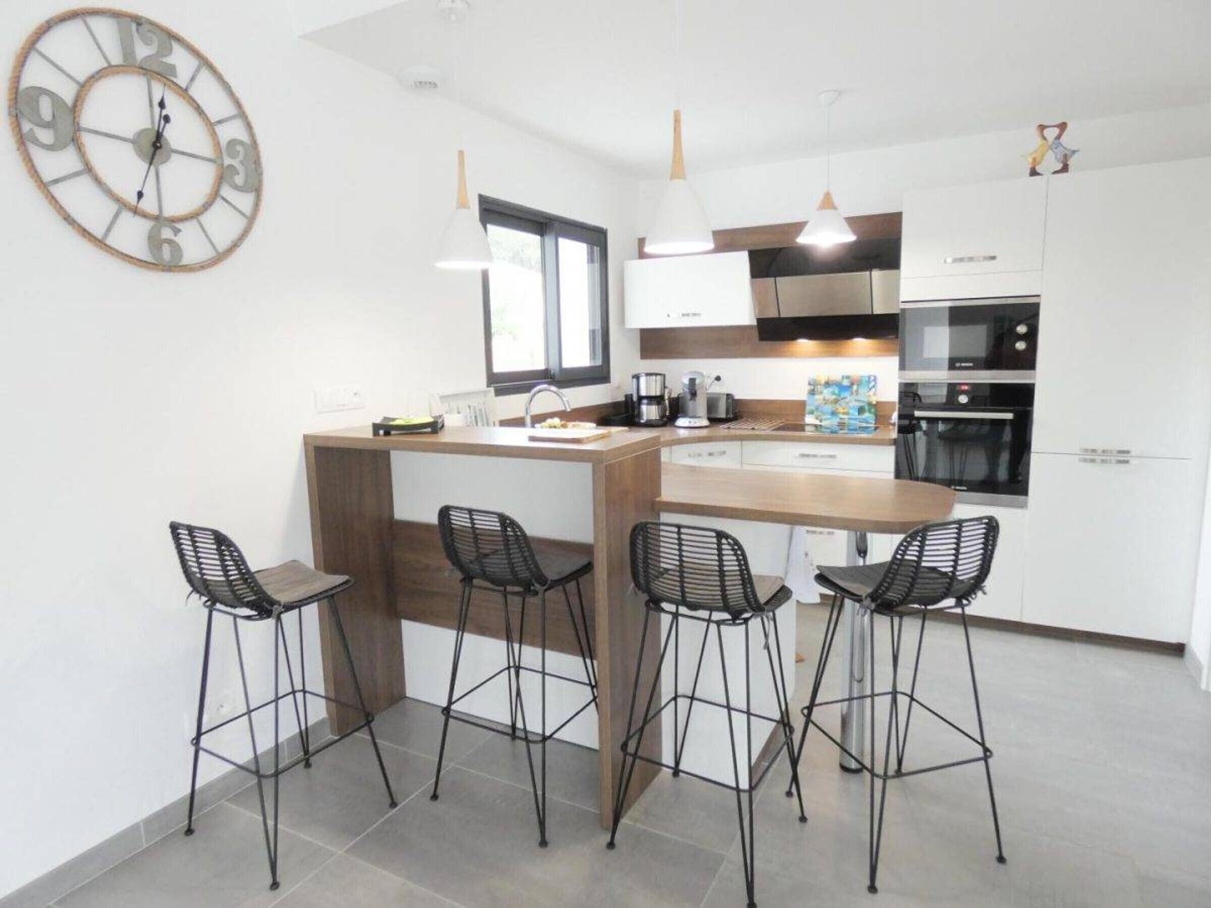 Una cocina moderna con una isla central, taburetes de bar y un reloj en la pared.
