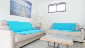 Ett vardagsrum med två beige soffor, ett soffbord, en tavla som föreställer en strand, en golvlampa och ett fönster.