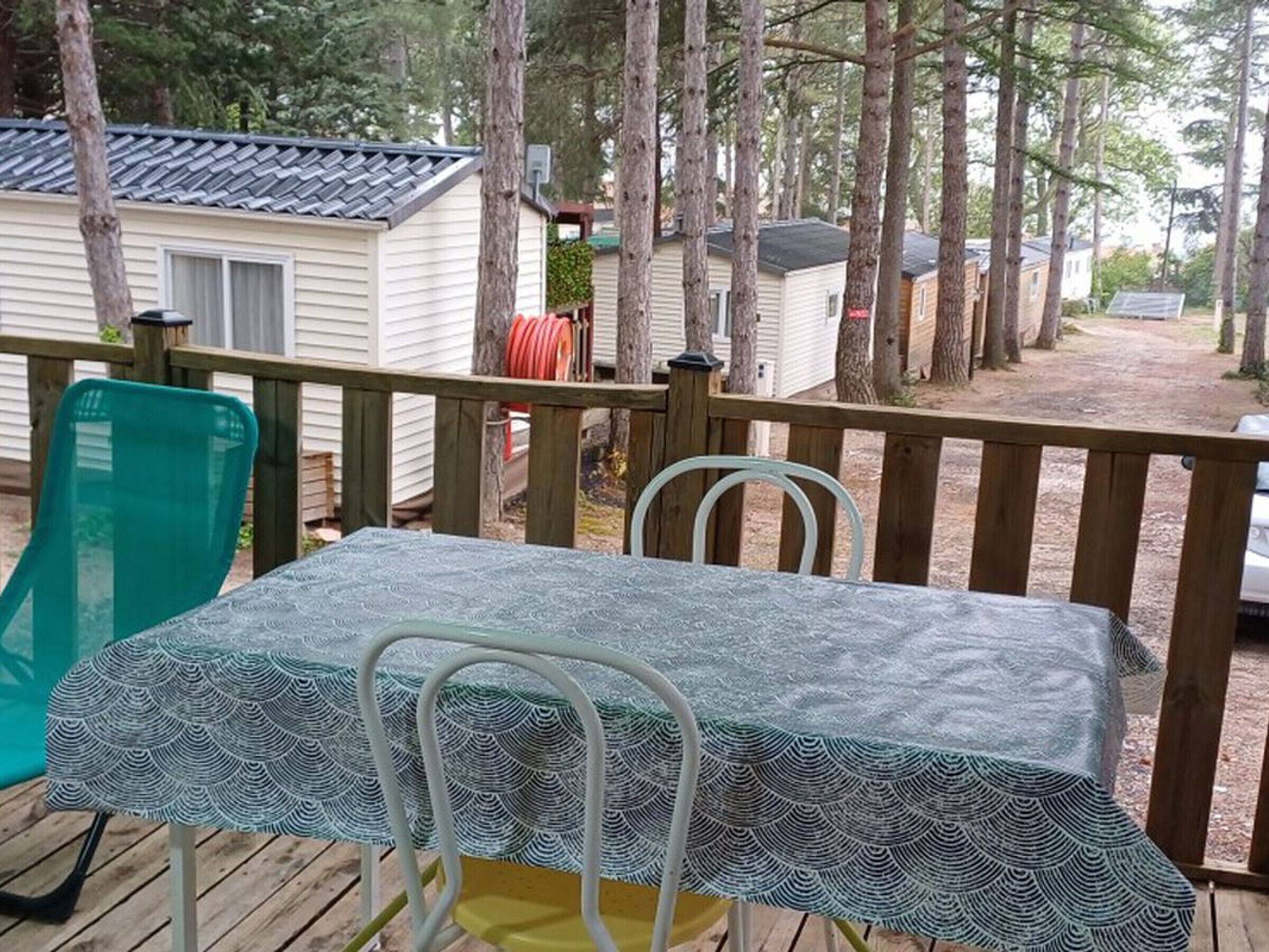 A deck with a table and chairs, surrounded by trees and mobile homes.