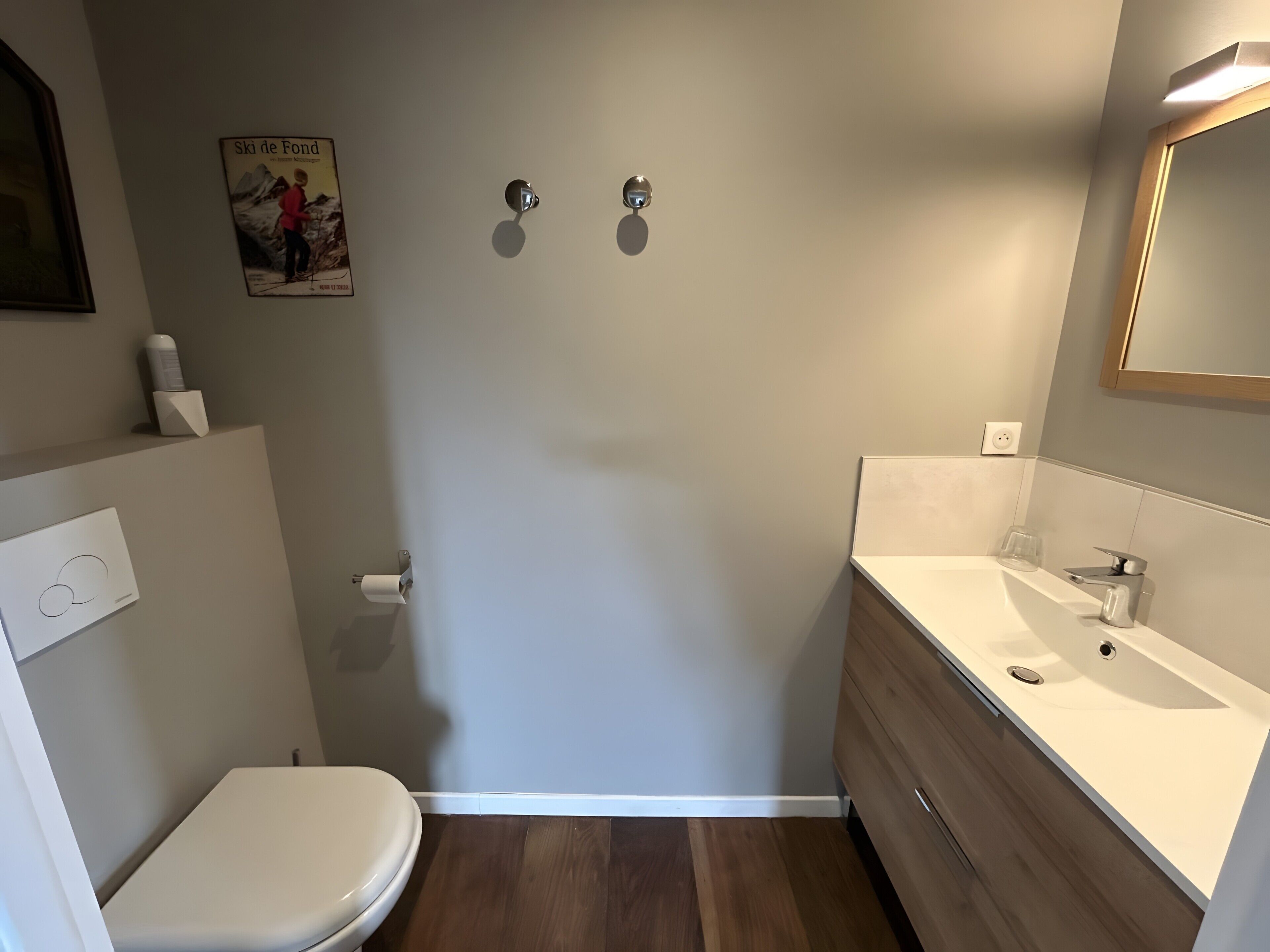 A bathroom with a toilet, sink, mirror, and a poster on the wall.