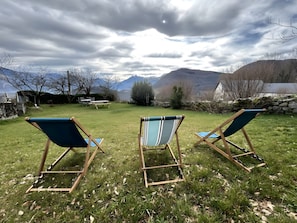 Drie houten ligstoelen met blauwe kussens in een gazon met uitzicht op bergen en een meer.