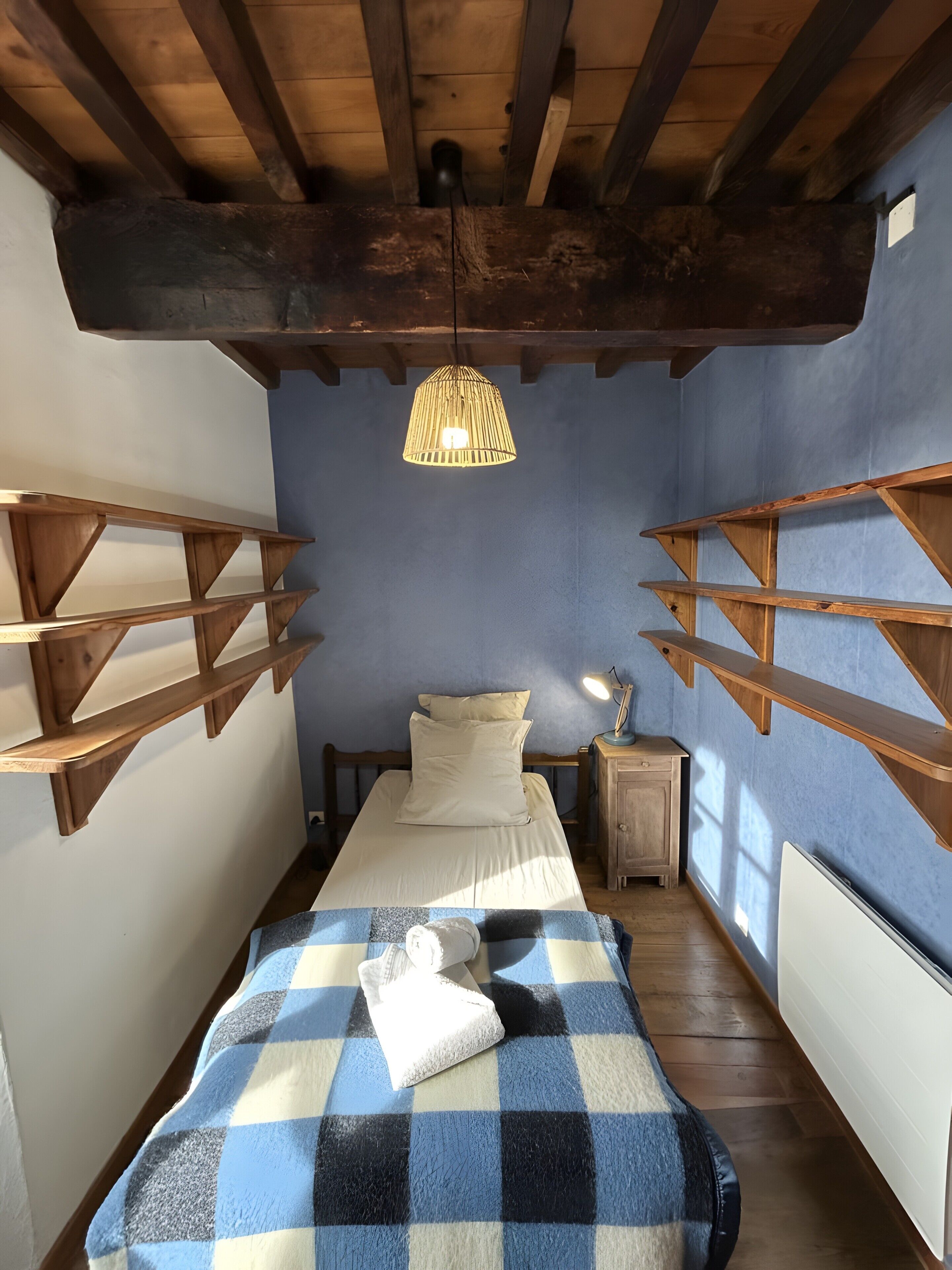 Ein Schlafzimmer mit einem Bett, Holzregalen, einer Hängeleuchte und einer Heizung.