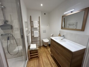 Een moderne badkamer met een douchecabine van glas, een houten trapje met handdoeken, een toilet en een wastafel met spiegel.