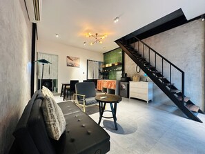 Ein modernes Wohnzimmer mit Sofa, Sesseln, einem Esstisch und einer Küchenzeile mit Treppe.