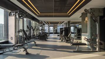 Une salle de sport moderne dotée de divers appareils d’exercice, de grandes fenêtres et d’un plafond haut.