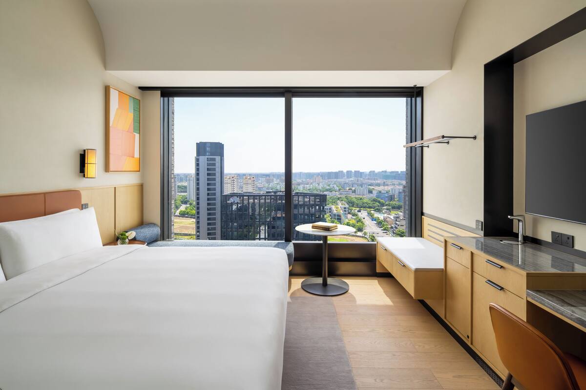 Una habitación de hotel con una cama grande, una mesita redonda pequeña, un sofá, un televisor y vistas a la ciudad.