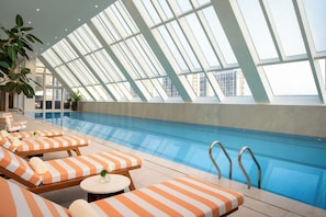 A modern indoor swimming pool with a high ceiling and skylights, surrounded by lounge chairs with striped cushions. - Jen Hangzhou By Shangri-La (Hangzhou)