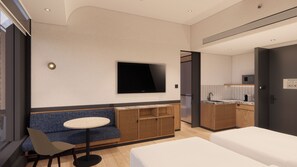 Una habitación de hotel moderna con sofá, una mesita redonda, televisor montado en la pared, kitchenette y cama.