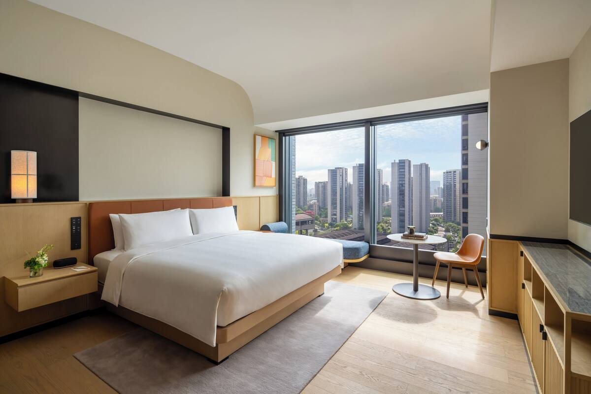 Habitación de hotel moderna con una cama grande, una mesita, una silla y vistas a la ciudad.