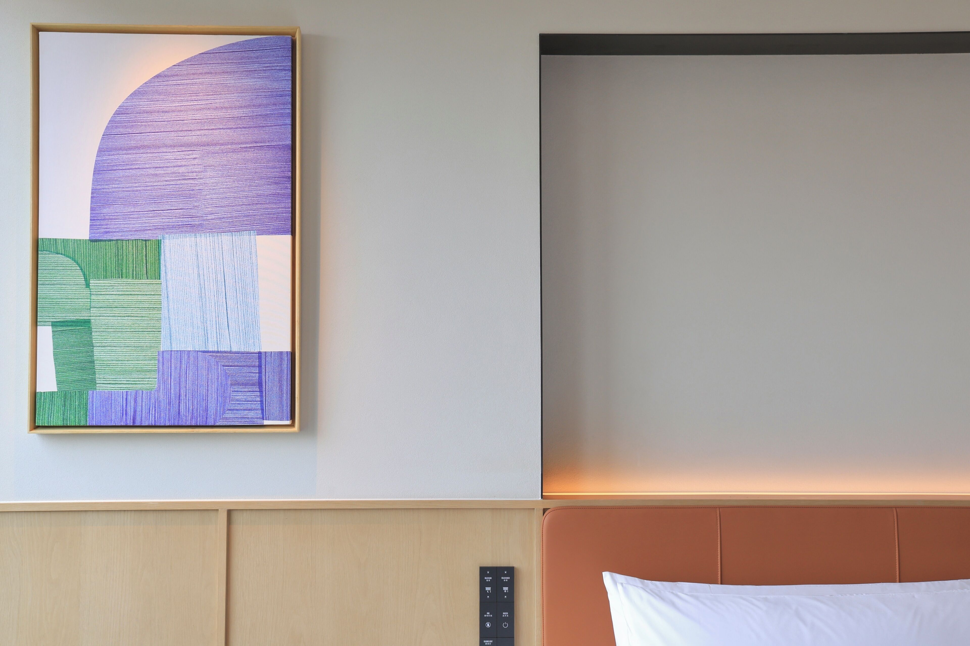 Habitación de hotel con cama, cabecero, panel de control en la pared y una obra de arte abstracta enmarcada.
