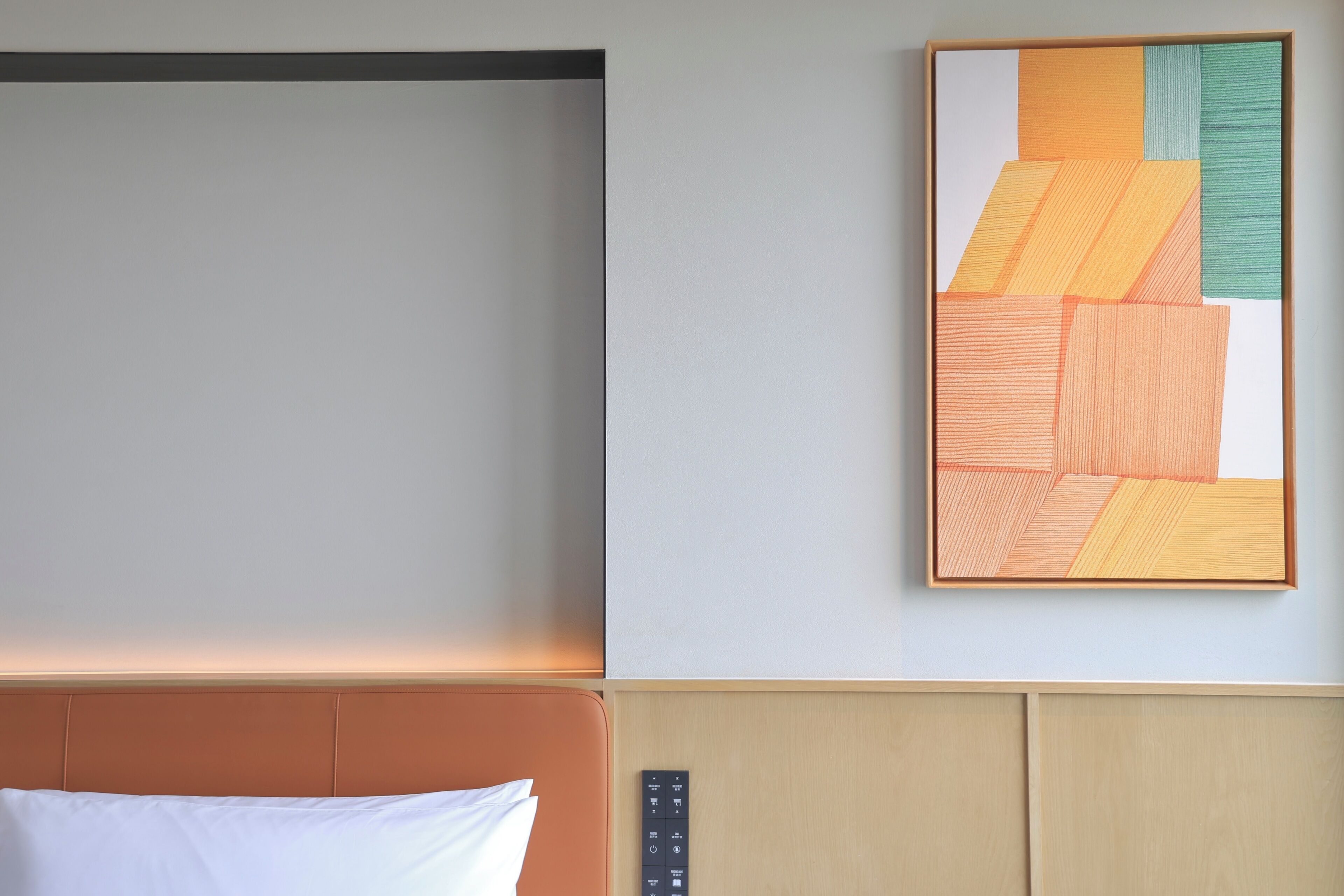 A hotel room with a bed, a headboard, a wall-mounted control panel, and a framed abstract artwork.