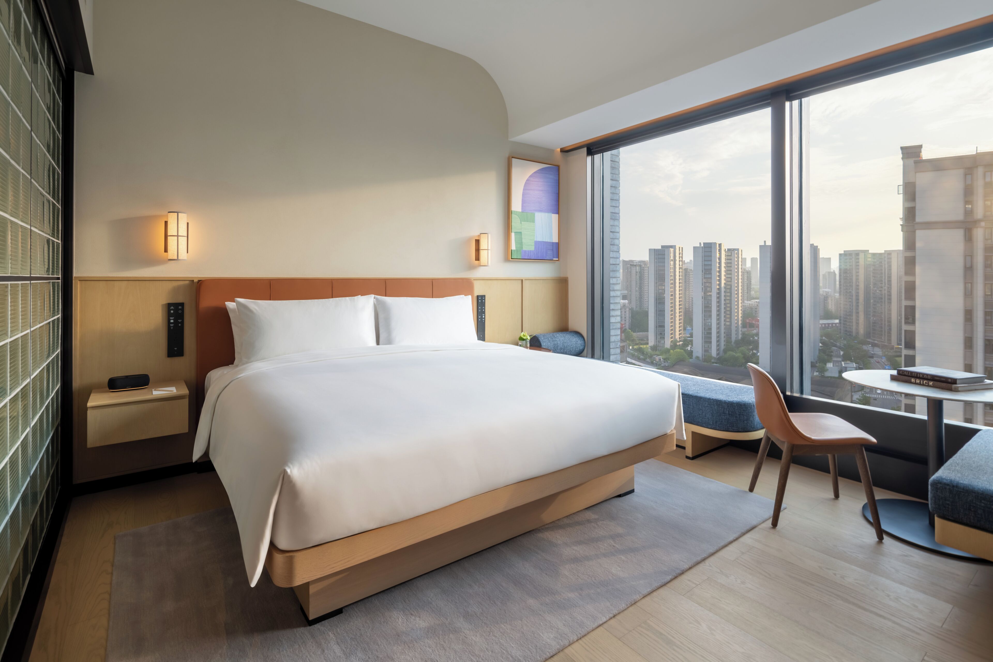 A modern hotel room with a large bed, a desk, and a view of the cityscape.