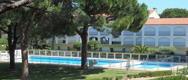 A hotel with a swimming pool, surrounded by trees and a building with balconies. - Charming apartment near the beach - 6 guests (Argelès-sur-Mer)