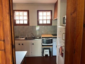 Eine kleine Küche mit Spüle, Mikrowelle, Backofen und einem kleinen Hocker.