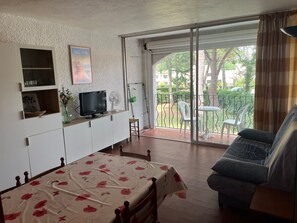 Ein Schlafzimmer mit Bett, Fernseher, kleinem Tisch, Sofa und einem Balkon mit Blick auf Bäume und ein Auto.