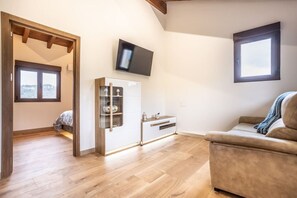 A room with a wooden floor, a sofa, a cabinet with glass doors, a television mounted on the wall, and a window. - Villa Camila 6 - La Panera (Villarraba)