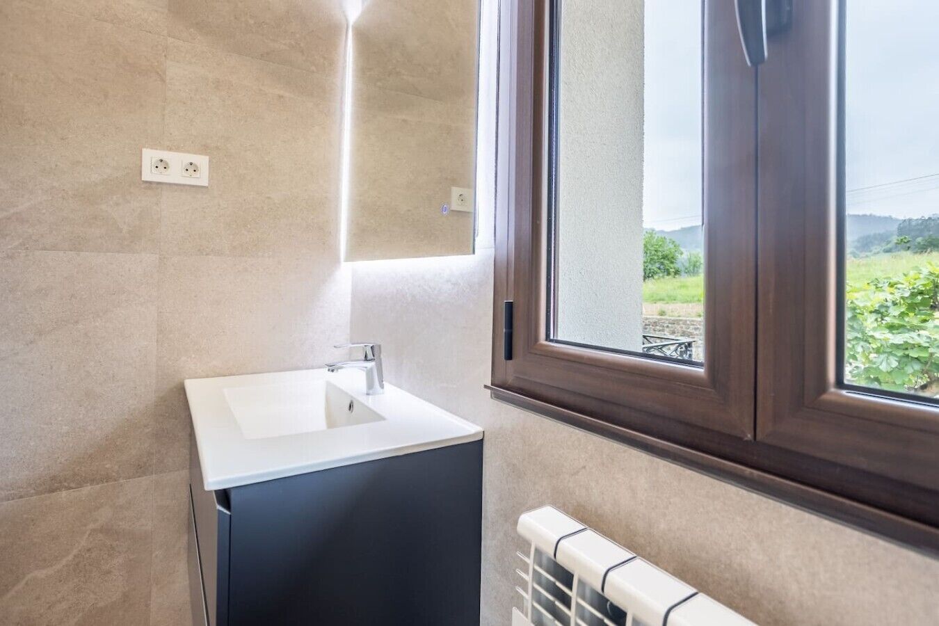 Een badkamer met een witte wastafel, een raam en een radiator.