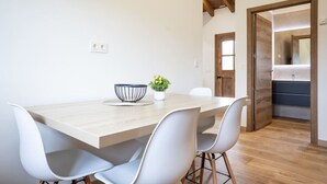 A modern dining area with a wooden table, white chairs, a black wire basket, and a potted plant. - Villa Camila 6 - La Panera (Villarraba)