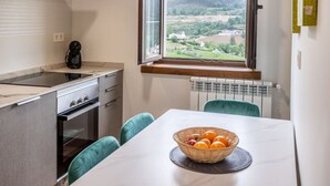 Une cuisine de taille réduite avec une fenêtre, une table sur laquelle se trouve un panier de fruits, et une vue sur la campagne.