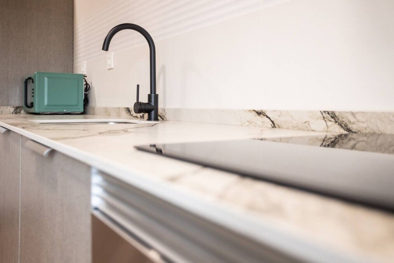 Una cocina con un grifo moderno, un electrodoméstico color aguamarina y una encimera de mármol.