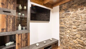 Une pièce avec un mur en pierre, des étagères en bois, un téléviseur à écran plat et un meuble de rangement intégré pour les appareils multimédias.