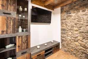A room with a stone wall, wooden shelves, a flat-screen TV, and a built-in entertainment unit.