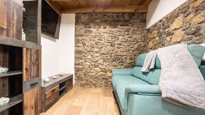 Une pièce chaleureuse avec un mur en pierre, un canapé de couleur turquoise, des étagères en bois et un plancher en bois.