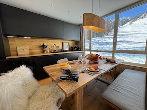 Eine moderne Küche mit dunklen Schränken, einer Holzausziehtafel und einem großen Fenster mit Blick auf Schnee.